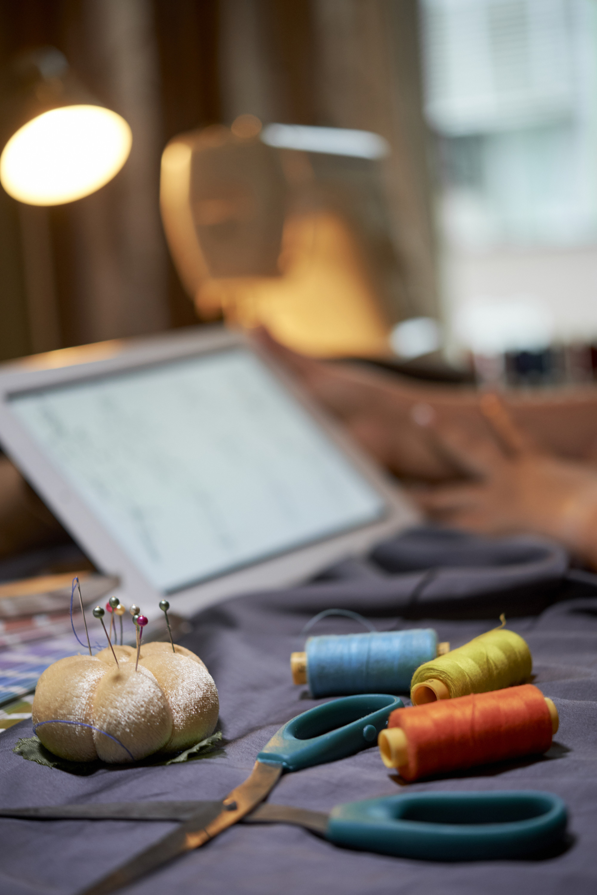 Workshop table with threads, needles and a tablet showing a design